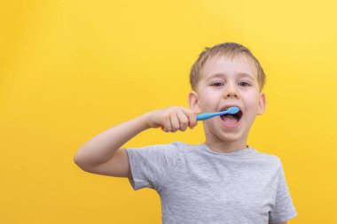 Tatlı sarışın çocuk dişlerini fırçalıyor ve sarı arka planda gülümsüyor. Boşluğu kopyala.