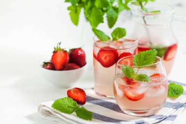 Ev yapımı taze çilekli limonata bardakta ve taze çilek ve nane yapraklı sürahi. Yaz içeceği 