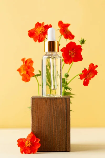 Serum, olej do pielęgnacji skóry twarzy na drewnianym podium otoczonym dzikimi kwiatami. Produkt do pielęgnacji kosmetycznej w kroplomierzu szkła. — Zdjęcie stockowe