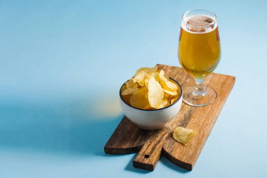 Bardakta soğuk light bira ve mavi arka planda tahta bir tahtanın üstünde doğal cips. Boşluğu kopyala.