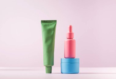 Kozmetik, krem, serum ve pembe arka planda jel gibi çok renkli kaplar. Boşluğu kopyala.