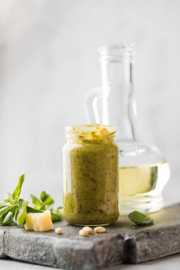 Yeşil fesleğen yapraklı pesto sosu, parmesan peyniri dilimleri ve tahta tahtada bir sürahi zeytinyağı. İtalyan mutfağı