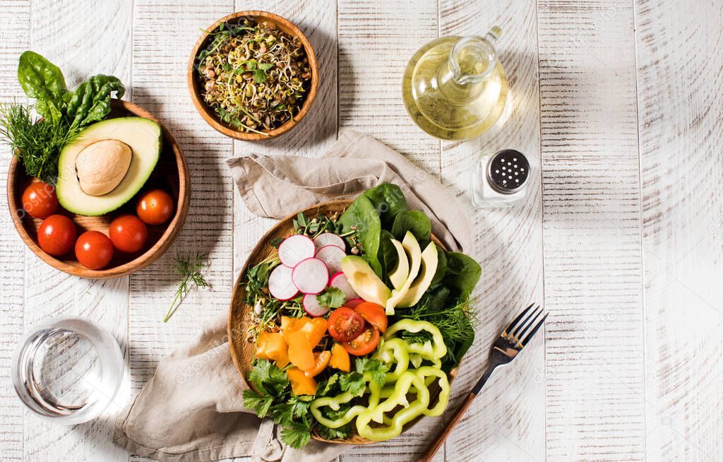 Vegetable summer salad with avocado, seasonal vegetables, spinach and micro-greens on a wooden white background. 