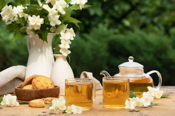 Teh Cina hijau dengan melati di cangkir dan teko teh di atas meja kayu dengan karangan bunga melati. — Stok Foto