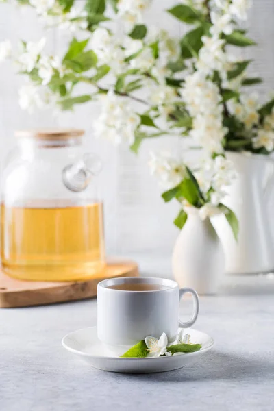 Secangkir teh hijau dengan melati di latar belakang teko teh dan cabang melati. — Stok Foto