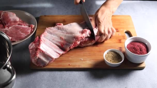 El chef divide las costillas de cerdo en trozos en una tabla de madera con un cuchillo — Vídeos de Stock