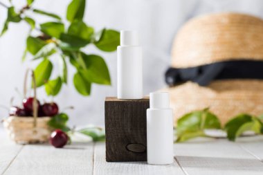 White tubes with cosmetics on a wooden podium against the background of leaves, cherry berries. Natural cosmetics. 