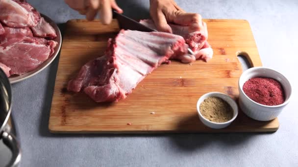 Der Koch teilt Schweinerippchen mit einem Messer auf einem Holzbrett in Stücke — Stockvideo