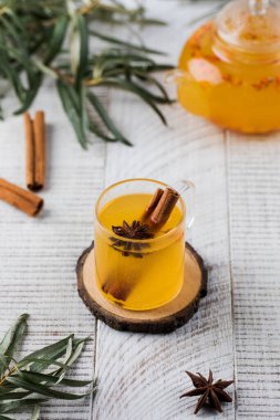 Beyaz ahşap arka planda tarçın çubuğu olan bir deniz dikenli kupada sonbahar çayı. Sonbahar havası.