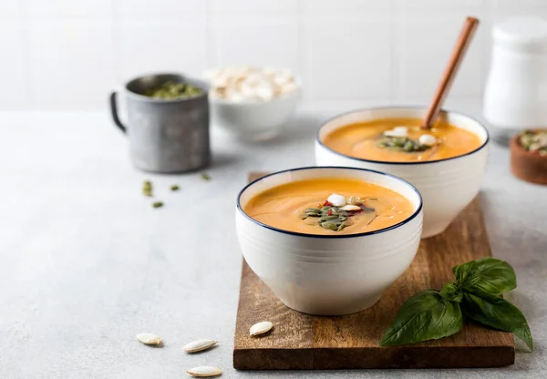 Dua mangkuk sup krim labu di papan kayu, ditaburi dengan biji. Sup musim gugur. Salin ruang. — Stok Foto