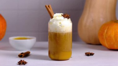 Bir kadın balkabağı lattesinin üzerine karamel şurubu döker ve üzerine tarçın serpiştirir..