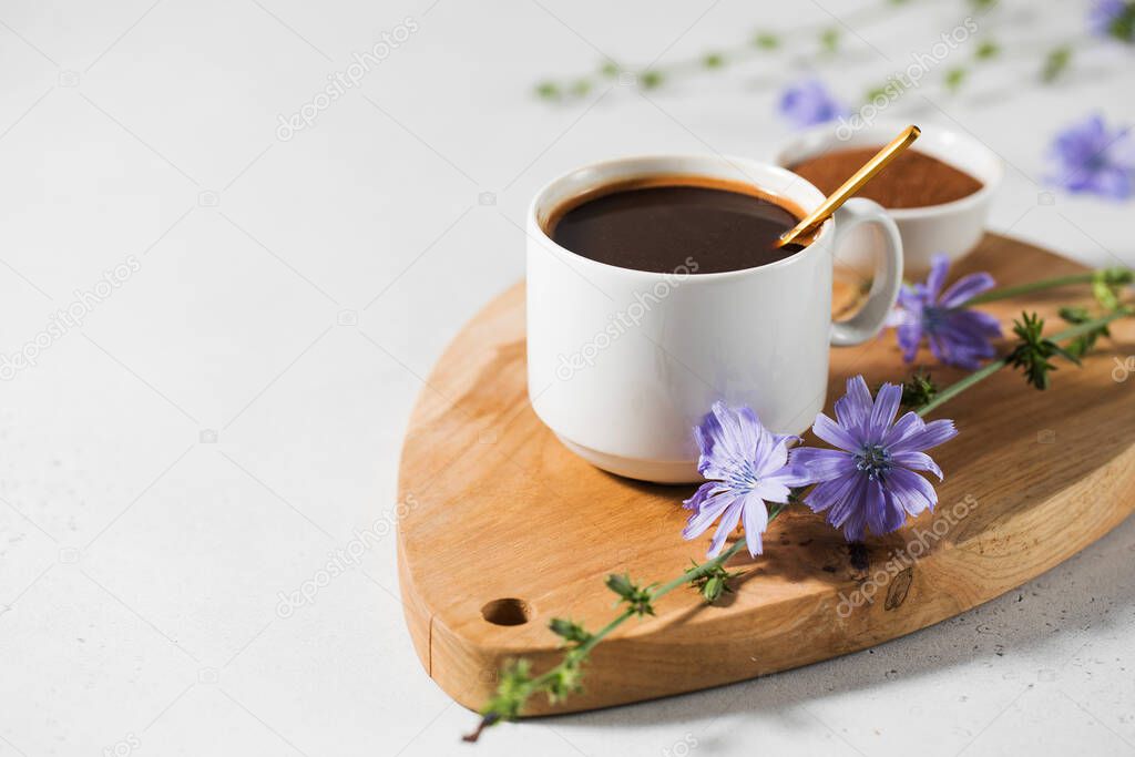 Chicory drink in a white mug with chicory flowers next to it on a wooden board.