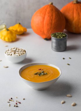 Beyaz bir tabakta kabak kremalı çorba ve kabak kabağı arkaplanındaki tohumlar. Sonbahar yemeği.