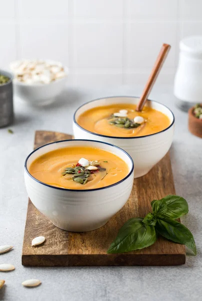 Dua mangkuk sup krim labu di papan kayu, ditaburi dengan biji. Sup musim gugur. — Stok Foto