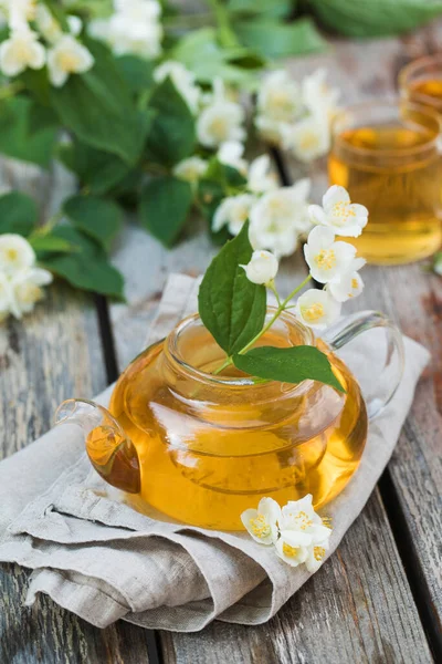 Teh Cina hijau dengan melati dalam pot teh di atas meja kayu dengan latar belakang bunga melati. — Stok Foto
