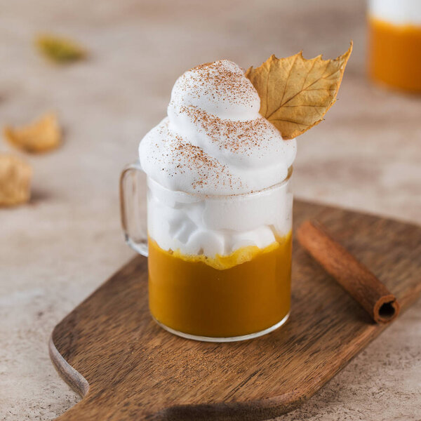 Mug of pumpkin coffee with whipped cream and dry leaf