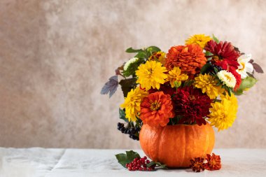 Bej duvarın yanındaki masada balkabağında bir buket taze çiçek.