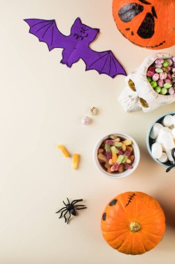 Cadılar Bayramı tasarımı, korkunç yüzlü balkabaklarıyla kağıt yarasa ve bej arka planda kopya alanı 