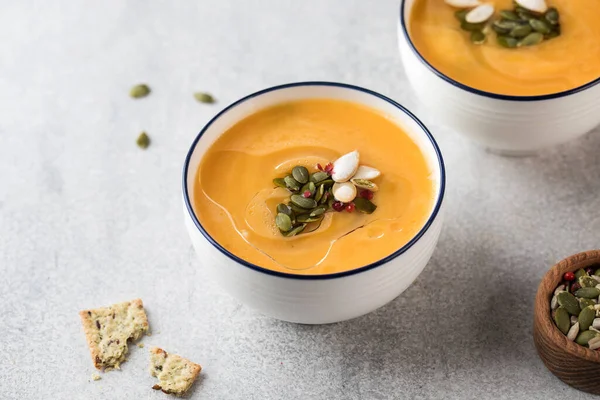 Dua mangkuk dengan sup krim labu dan biji labu dengan latar belakang abu-abu. Pemandangan bagus. Resep Musim Gugur. — Stok Foto