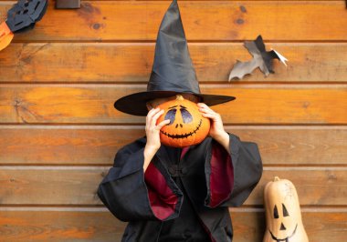 Büyücü kostümlü çocuk yüzünde ürkütücü bir balkabağı tutuyor.