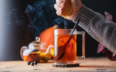 Bir kadın bir kupa çaya limon suyu sıkıyor. Sonbahar rahat kompozisyonu.