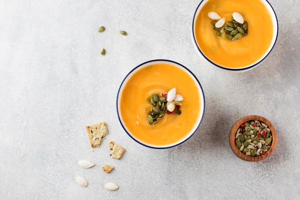 Dua mangkuk dengan sup krim labu dan biji labu dengan latar belakang abu-abu. Pemandangan bagus. Resep Musim Gugur. — Stok Foto