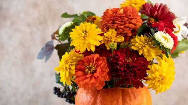Bouquet of fresh flowers in pumpkin on table near beige wall — Stock Photo, Image