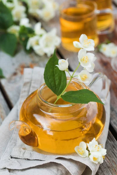 Teh Cina hijau dengan melati dalam pot teh di atas meja kayu dengan latar belakang bunga melati. — Stok Foto