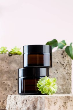 Doğal kozmetik ürünleri olan kavanozlar ve pembe üzerindeki beton tabaklarda sulandırıcılar.