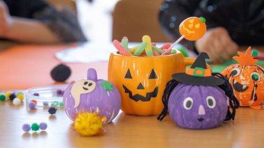  Colorful Halloween decorations, crafts and candy in a pumpkin-shaped mug on a table. Halloween celebration concept.