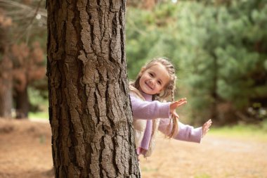 Joyful child playing peekaboo in forest during autumn adventure. Concept of family and nature