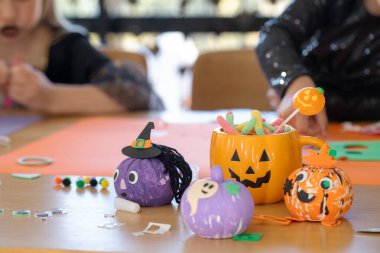  Colorful Halloween decorations, crafts and candy in a pumpkin-shaped mug on a table. Halloween celebration concept.
