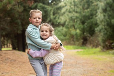  A touching embrace between a brother and sister on a trail in a pine forest. Family concept, happy siblings