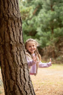 Joyful child playing peekaboo in forest during autumn adventure. Concept of family and nature