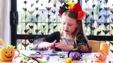 Caucasian young girl crafting at halloween themed table with colorful flower crown. The concept of childrens crafts for Halloween. Young girl decorates festive mask with playful enthusiasm