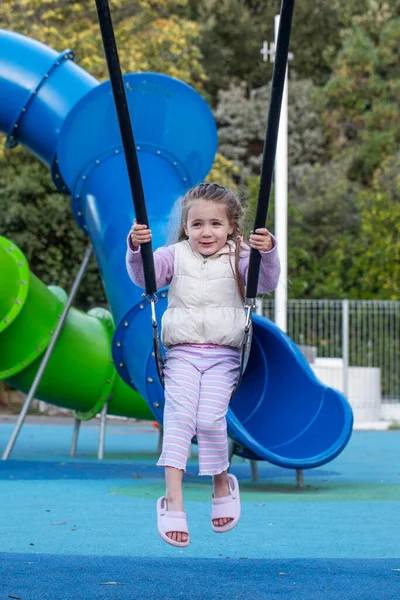 Güneşli bir günde parkta sallanan sevimli küçük bir kız. Mutlu çocuk dışarıda eğleniyor ve yaz eğlencesi.