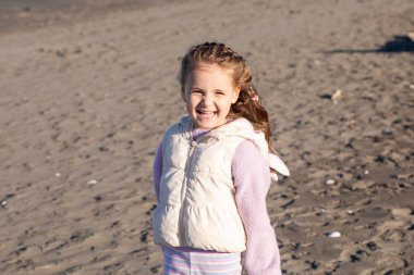Mutlu çocuk kumsalda güneşli bir günün tadını çıkarıyor, gülümsüyor ve okyanus dalgalarının yanında oynuyor. Parlak doğal ışık ve ılık tonlar çocukluğun kaygısız ruhunu yakalar.
