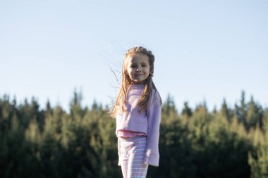 Neşeli çocuk güzel bir orman manzarasında dışarıda oyun oynamaktan zevk alıyor. Resim, doğayla, uzun ağaçlarla çevrili çocukluk macerasıyla, özgürlüğü, mutluluğu ve bağlantıyı taşır.