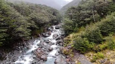 Yeni Zelanda 'da yağmurda güzel bir dağ nehrinin üzerinde alçaktan uçuyorum. Doğa manzarası. Hava turkuaz şelalesi yosunlu kayalıklardan ve yemyeşil alt kattan aşağı düşüyor.