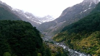 Kayalık arazide şelale gibi akan görkemli bir nehrin hava manzarası dramatik bulutlu bir gökyüzü altında yemyeşil vadilere. Manzaralı Yeni Zelanda vahşi doğası, doğa ve seyahat kavramı.