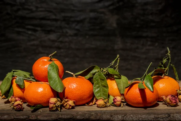 Koyu taş zemin üzerinde yaprakları olan mandalinalar, kırsal ahşap masa üzerinde