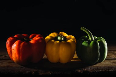 Üç farklı renkte biber, kırmızı, yeşil ve sarı kırsal bir ahşap masa üzerinde siyah bir arka plan.