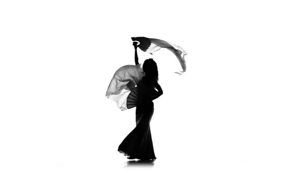 Экзотическая танцовщица живота, трясущая бедрами, использует два вентилятора на белом, замедленном движении, силуэт — стоковое видео