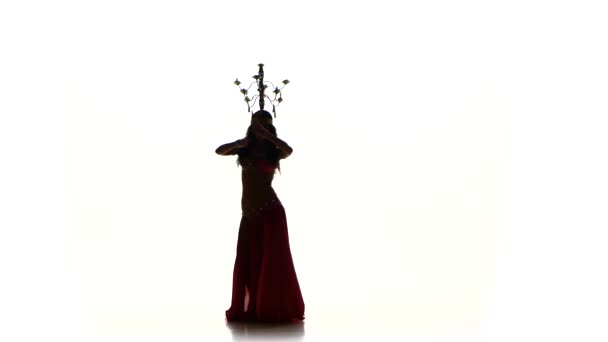 Attraktiva magdansös dans med ljus på huvudet, skakar hennes höfter, silhouette, på vitt — Stockvideo