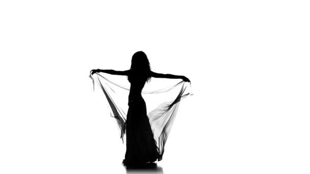 Pretty young woman starts dancing belly dance with shawl, sihouette, on white, slow motion — Stock videók