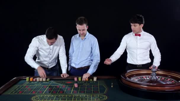 Young man playing roulette in the casino. Dealer takes bets. Black — Wideo stockowe