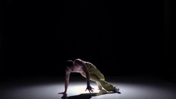 Танцюючий чоловік в жовтих штанях з голим торсом починає танцювати на чорному, тіні, повільному русі — стокове відео