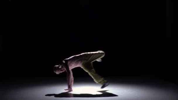 Человек-брейкдансер в желтых брюках начинает делать стойку на руках на черном, тени, замедленном движении — стоковое видео