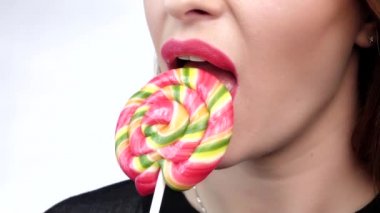 Woman licking a color shiny lollipop, against white background. Close up. Slow motion