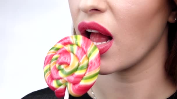 Woman licking a color shiny lollipop, against white background. Close up. Slow motion — ストック動画